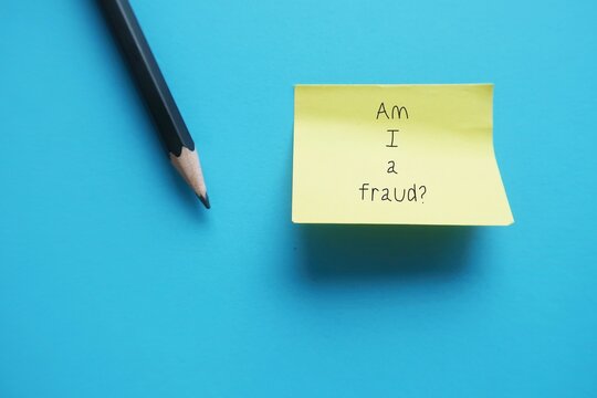 Stick note on blue background with text AM I A FRAUD? concept of IMPOSTER SYNDROME, feeling of doubt one own skills, talents or accomplishments and have internalized fear of being exposed as fraud