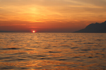 Sunset over the sea, orange sun in the clouds on the horizon, sea coast of Croatia, Dalmatia, Brela