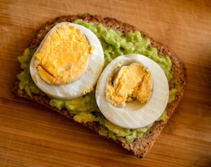  avocado toast topped with a perfectly boiled egg, presented on a rustic wooden board