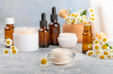 Fototapeta na wymiar Chamomile spa. Composition with chamomile flowers, handmade soap, essential oil cosmetic bottle, body cream, scrub and sea salt on a white texture background. Relaxing beauty treatments.Copy space