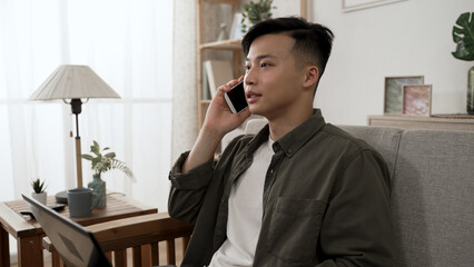 cheerful asian male startup owner receiving important business call from customer and talking while working from home on the computer.