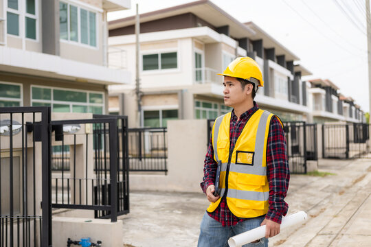 Young Asian engineer inspects architecture, construction project concept, young professional engineer in helmet and blueprint paper at house construction site.