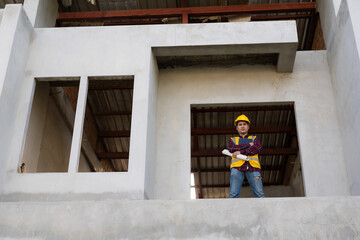 Young Asian engineer inspects architecture, construction project concept, young professional engineer in helmet and blueprint paper at house construction site.