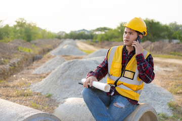 Young Asian engineer inspects architecture, construction project concept, young professional engineer in helmet and blueprint paper at house construction site.