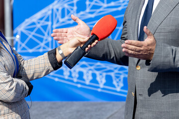 Female journalist holding microphone making media interview with male unrecognizable person