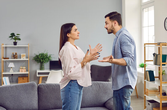 Emotional stressed young couple having argument at home. Portrait of angry irritated man and woman talking and looking at each other with annoyed. Relationship problems, family conflicts