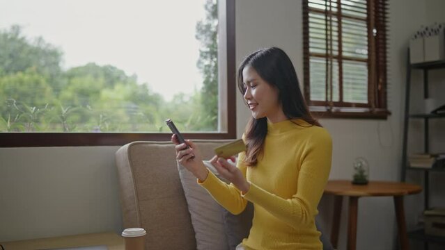 Yellow sweater woman is using credit card for shopping online on the mobile phone at home.