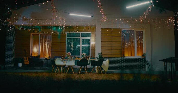 Beautiful cottage house with festive illuminations on facade and table in yard in summer, 4K, Prores