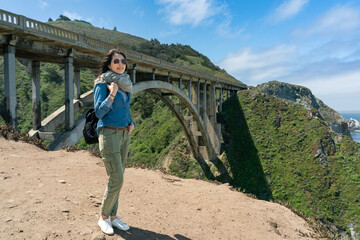 full length of fashionable asian Korean girl admiring natural beauty with backdrop of big sur bridge in California usa