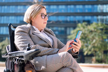 businesswoman using wheelchair using mobile phone outdoors at the financial district, concept of...