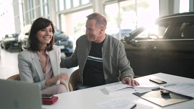 Middle aged couple closing the deal with a salesmen on their new car at the dealership