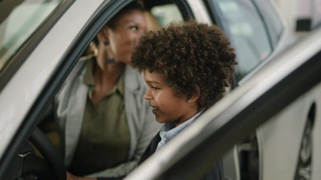 Young African American woman testing out the vehicle she desires with her son at the car dealership
