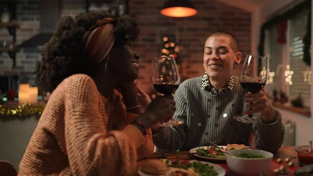 Young mixed lesbian couple having wine and dinner together in their home decorated for the Christmas holidays