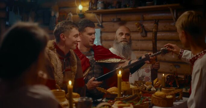 ancient Slavic people dining in old wooden house, warrior showing his steel sword, 4K, Prores