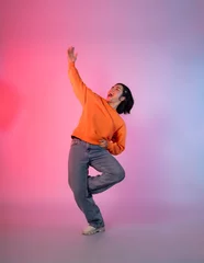 Deurstickers Image of a young Asian person dancing on a neon colored background © 1112000