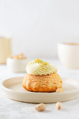Shu cake with pistachio cream, French dessert with a cup of coffee on a table.