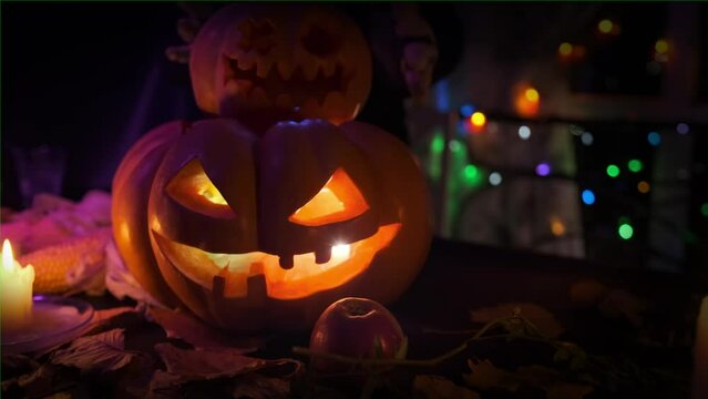 Two carved festive pumpkins touch the hands of a witch and a laughing skeleton skull during a Halloween night party. Beautiful festive Halloween background