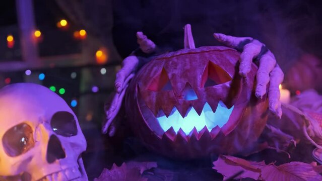 The devil's scary paws caress Jack-O-Lantern as he walks through the cemetery on a grave next to a skull on Halloween night