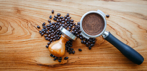 Top view of equipment in a coffee shop of barista coffee tool portafilter with tamper and dark roasted coffee beans on wooden background