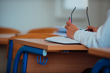 A close-up a student in a classroom holding glasses in her hand while focusing on her academic...