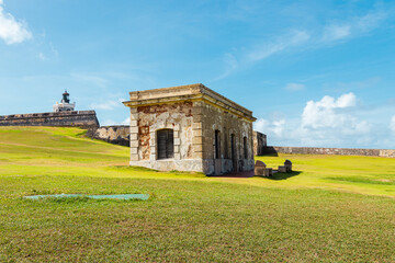 old stone structure in the middle of a green field from el morro with the san felipe castle behind...