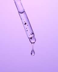 Drops of cosmetic serum and a pipette. A skin care product. Purple background. 