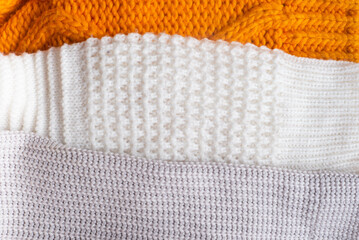 Handmade orange and white chunky knit sweaters lie against a background of textured linen. High...
