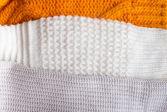 Handmade orange and white chunky knit sweaters lie against a background of textured linen. High quality photo