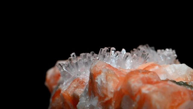 Clear Natrolite crystals on Orange Gmelinite (from Little Deer Park Quarry, Glenarm, N. Ireland) sample rotating slowly against a black background. 