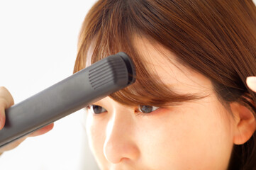 ヘアアイロンでヘアメイクをする若い女性