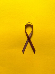 Brown ribbon on yellow background, cancer awareness, World Cancer Day, World Autism Awareness Day