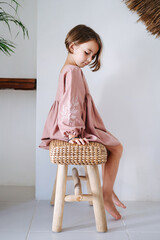 Child modestly sitting on a wooden chair, side view