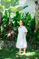 Barefoot girl in a white dress stands in a tropical garden