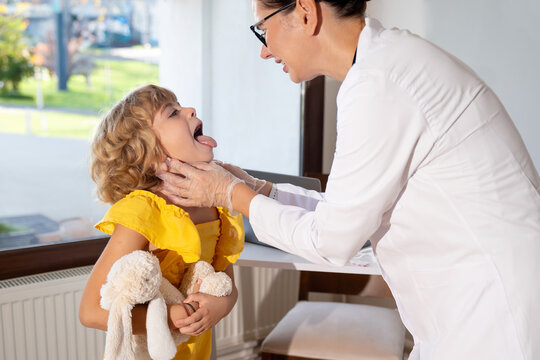 Female doctor checking child's exam kid throat during medical checkup in medical exam room at the clinic. Friendly pediatrician using stethoscope to examine breathing and heartbeat of young patient