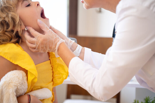 Female doctor checking child's exam kid throat during medical checkup in medical exam room at the clinic. Friendly pediatrician using stethoscope to examine breathing and heartbeat of young patient