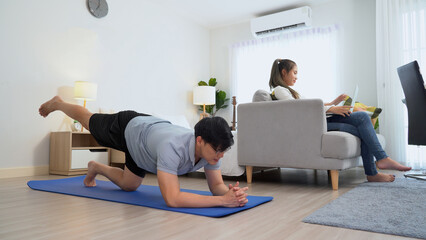 happy asian young man doing exercise and watching tutorial on laptop with mat in living room at...
