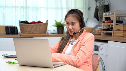 asian young business woman using laptop with headphones meeting to video conference remote work in in living room at home . Asia female teen student learning online training class. education at home.