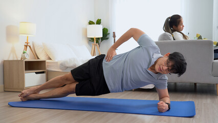 happy asian young man doing exercise and watching tutorial on laptop with mat in living room at...