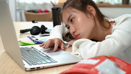 Tired asian young business woman sleepy using laptop working at home . bored Asia female teen student learning online lying on desk . lazy education at home.