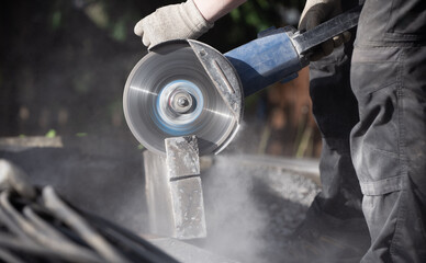 Detail of a man at work with an angle grinder sawing a stone outdoors