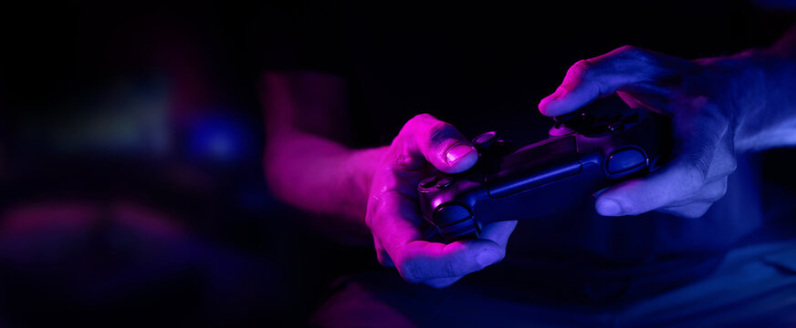 closeup of wireless video game controller in gamer hands in neon lights. banner with copy space