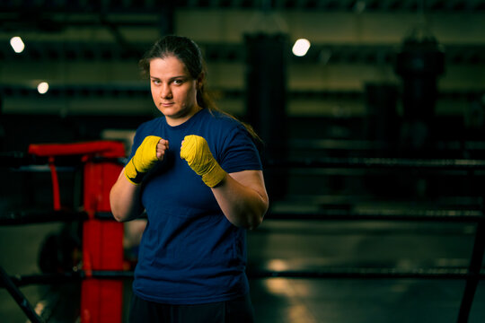 portrait focused Boxer girl in yellow boxing bandages standing in a boxing stance on a dark background in a gym before a fight