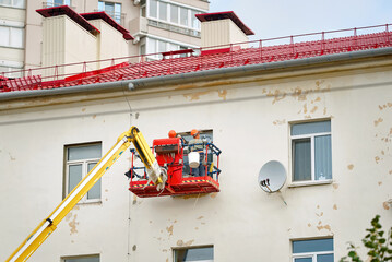 Two workers in cradle at height plastering window jamb, apply wall putty and levelling wall....