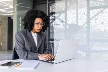 Worried young African American businesswoman working on laptop in office, looking upset at laptop...