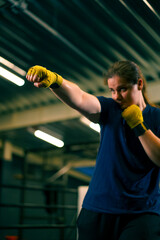 portrait focused Boxer girl in yellow boxing bandages standing in a boxing stance on a dark...