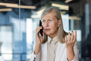 Close-up photo. Worried and upset senior business woman talking on the phone in the office and...