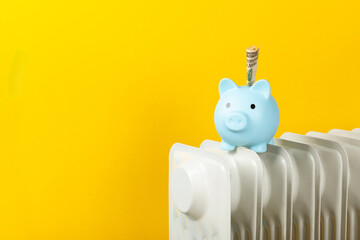 Savings concept.Money in piggy bank on radiator on yellow wall background. Concept of heating season. Concept of expensive heating costs and rising energy bill prices for winter cold season