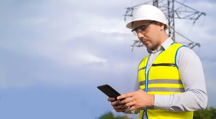 male engineer, power engineer in a helmet checks a power line using a tablet online. Electrician...