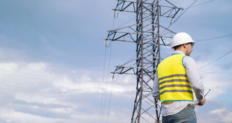 Caucasian male engineer in a helmet and safety glasses uses a smartphone for field work near a telecommunications tower that controls cellular electrical installations.