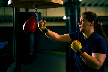 a girl boxer in gloves works out the strength of blows and coordination on a small punching bag in...